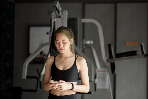 beautiful-smiling-woman-using-phone-while-gym-fitness-technology-concept