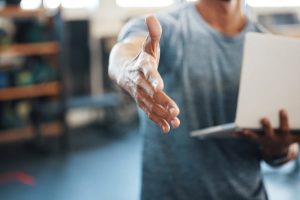 congrats-signing-up-with-us-closeup-shot-unrecognisable-man-extending-handshake-while-using-laptop-gym